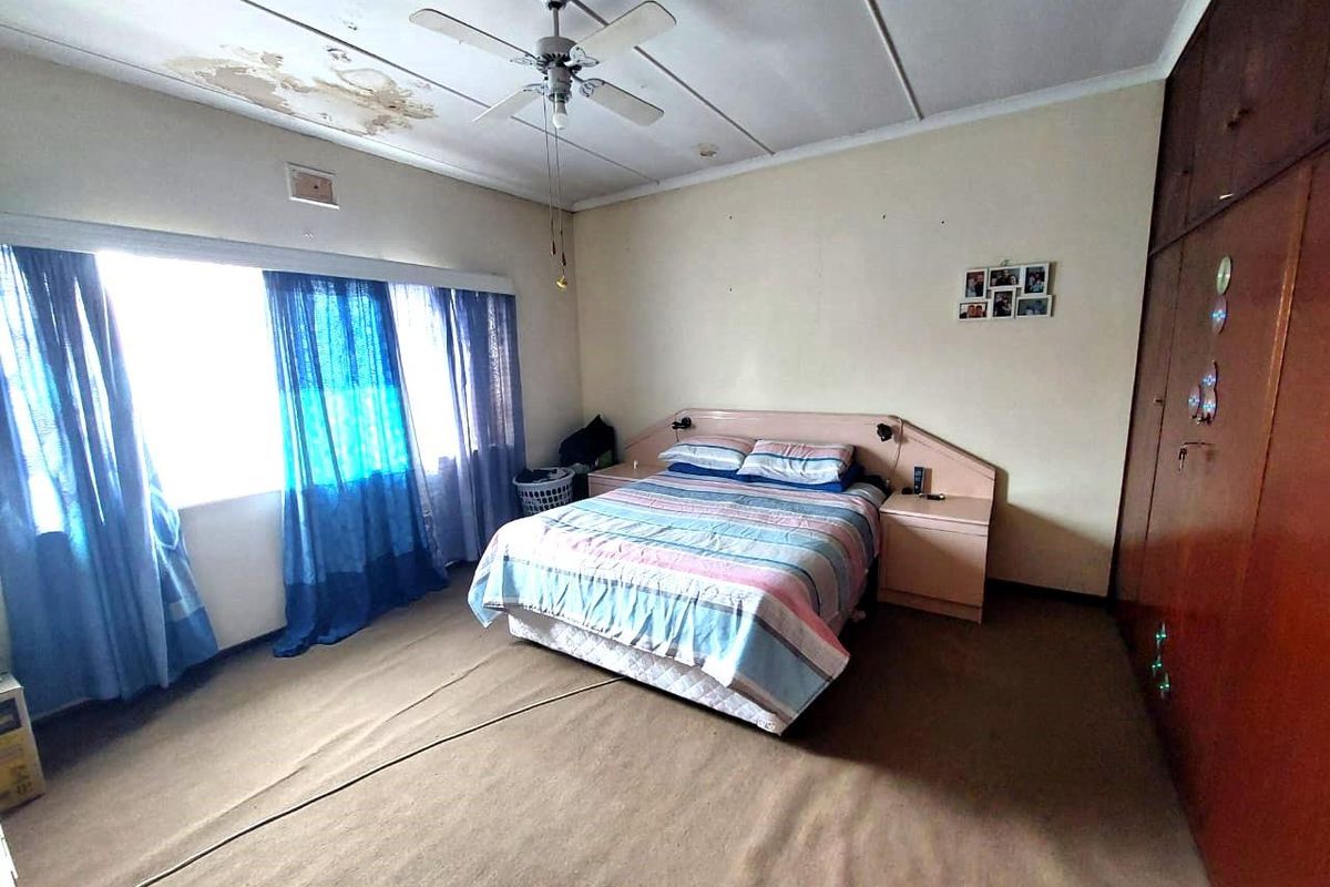 Spacious bedroom featuring built-in wooden cabinetry, a ceiling fan, and large windows. The room requires ceiling repairs and flooring updates.