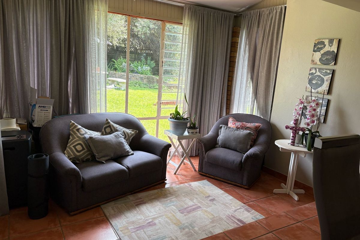 A cozy living area featuring terracotta floor tiles and large windows that provide natural light and views of the garden.