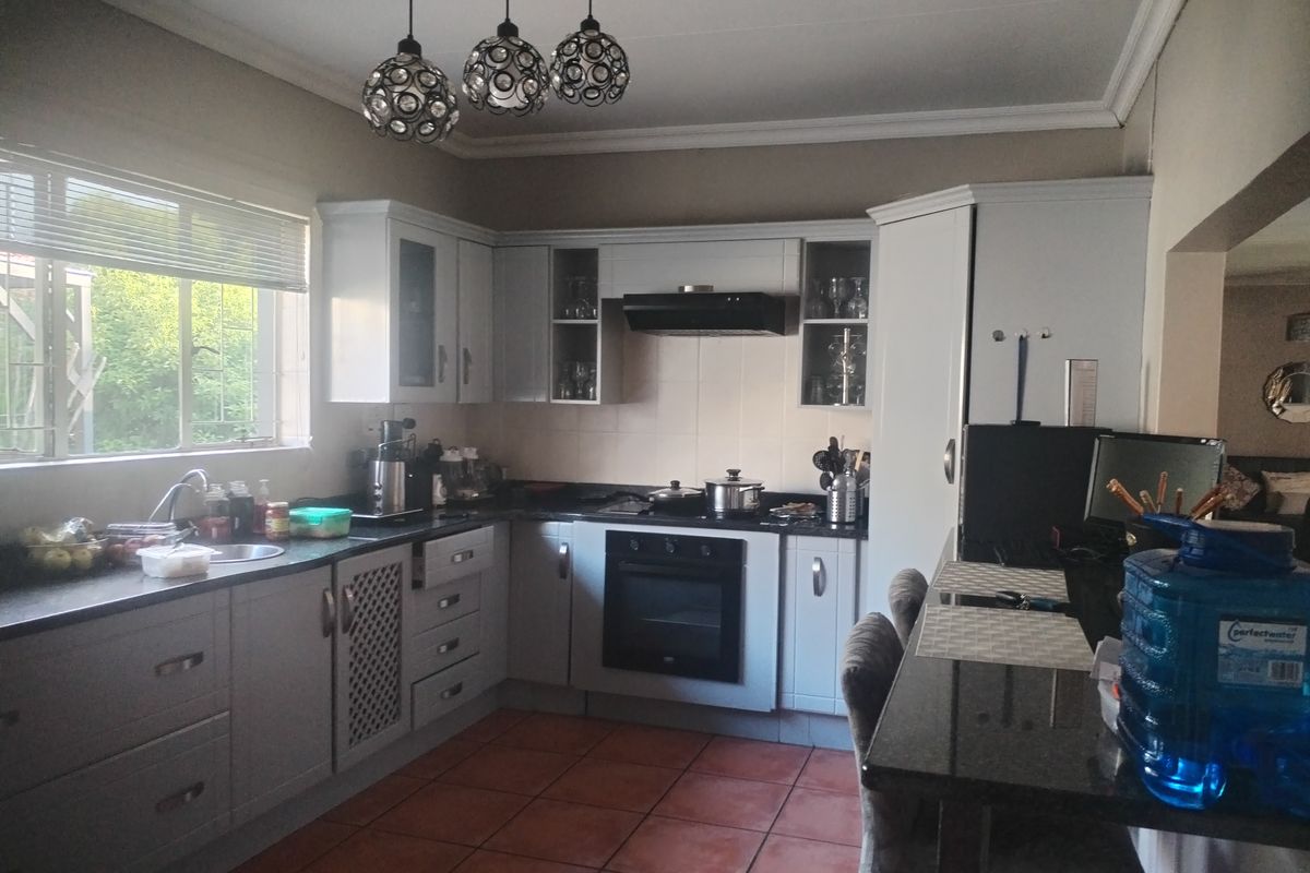 A functional kitchen featuring light-toned cabinetry, dark granite countertops, a built-in oven, extractor fan, and tiled flooring with a breakfast bar area.