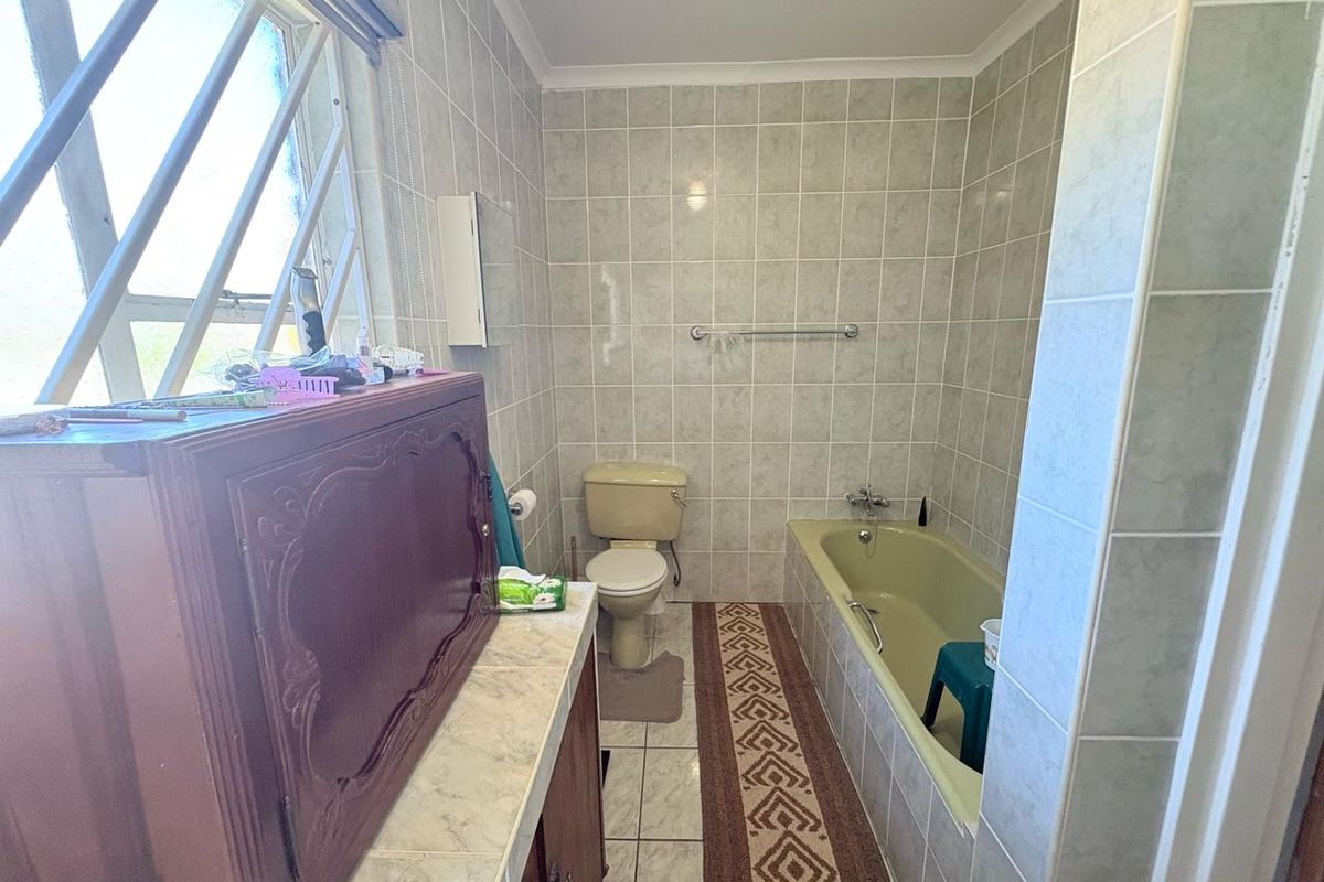 A dated bathroom featuring a built-in bathtub, toilet, and vanity unit with tiled walls and flooring.