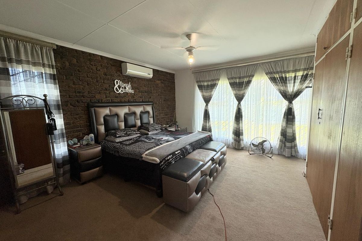 Spacious bedroom featuring a textured brick feature wall, split-system air conditioning, large windows with natural light, and built-in wardrobe storage.