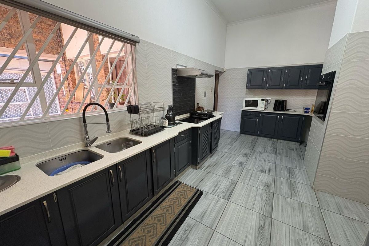 Modern kitchen featuring dark cabinetry, stone countertops, double basin sink, built-in oven, and hob with extractor fan, complemented by tiled flooring.
