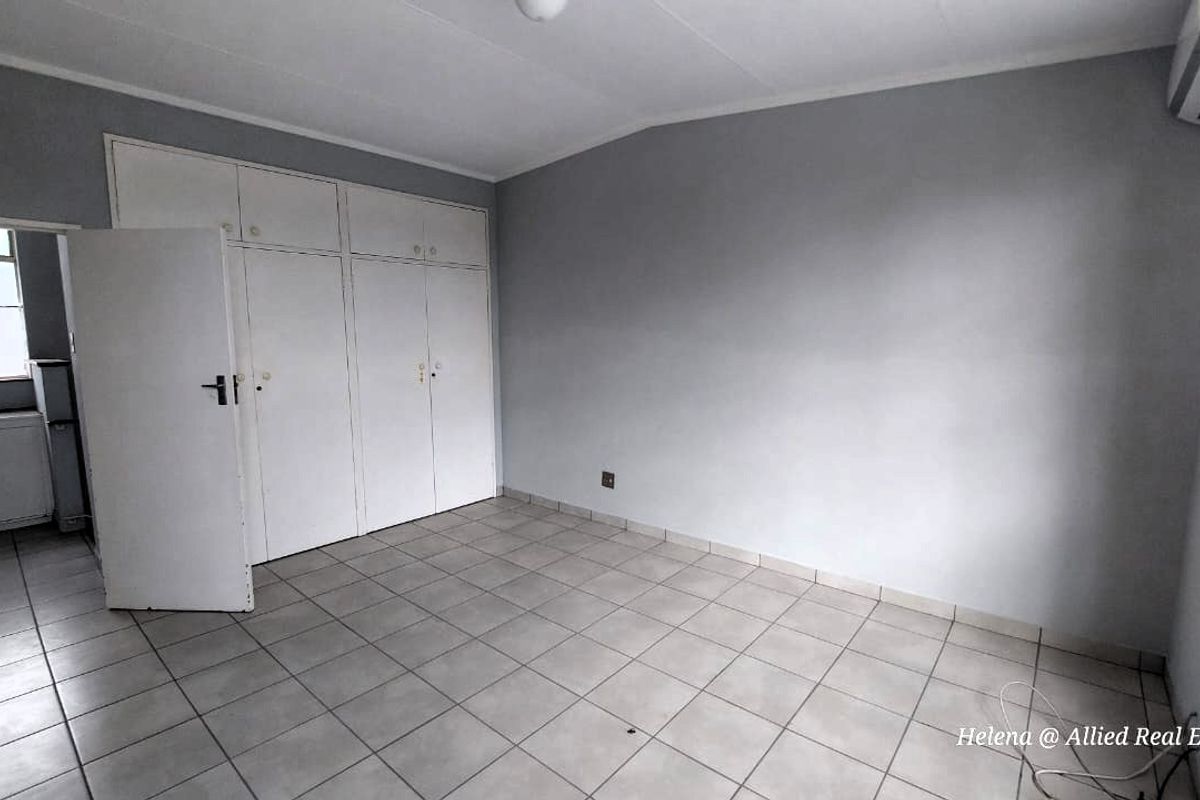 A vacant bedroom featuring built-in cupboards, tiled flooring, and a wall-mounted air conditioning unit.