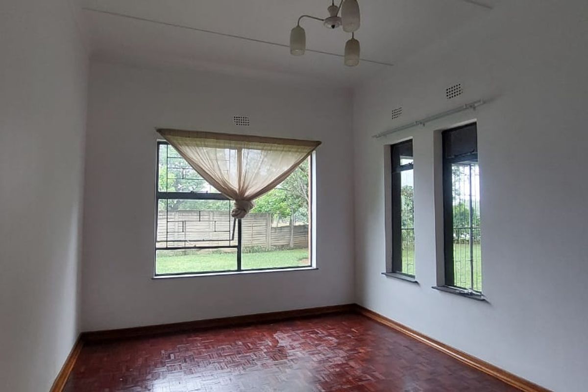 A bright, empty living room featuring traditional parquet flooring, large windows with security bars, and neutral wall finishes.