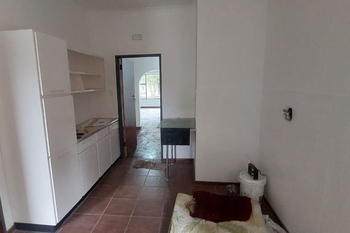 A basic kitchen area featuring white cabinetry, tiled flooring, and a doorway leading to an adjacent room.