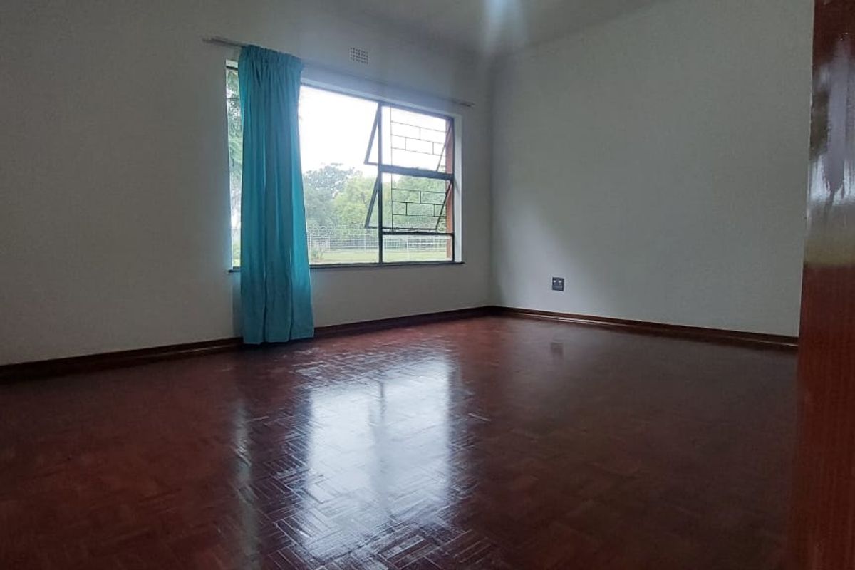 A bright, empty bedroom featuring polished parquet wooden flooring and a large window with security bars.