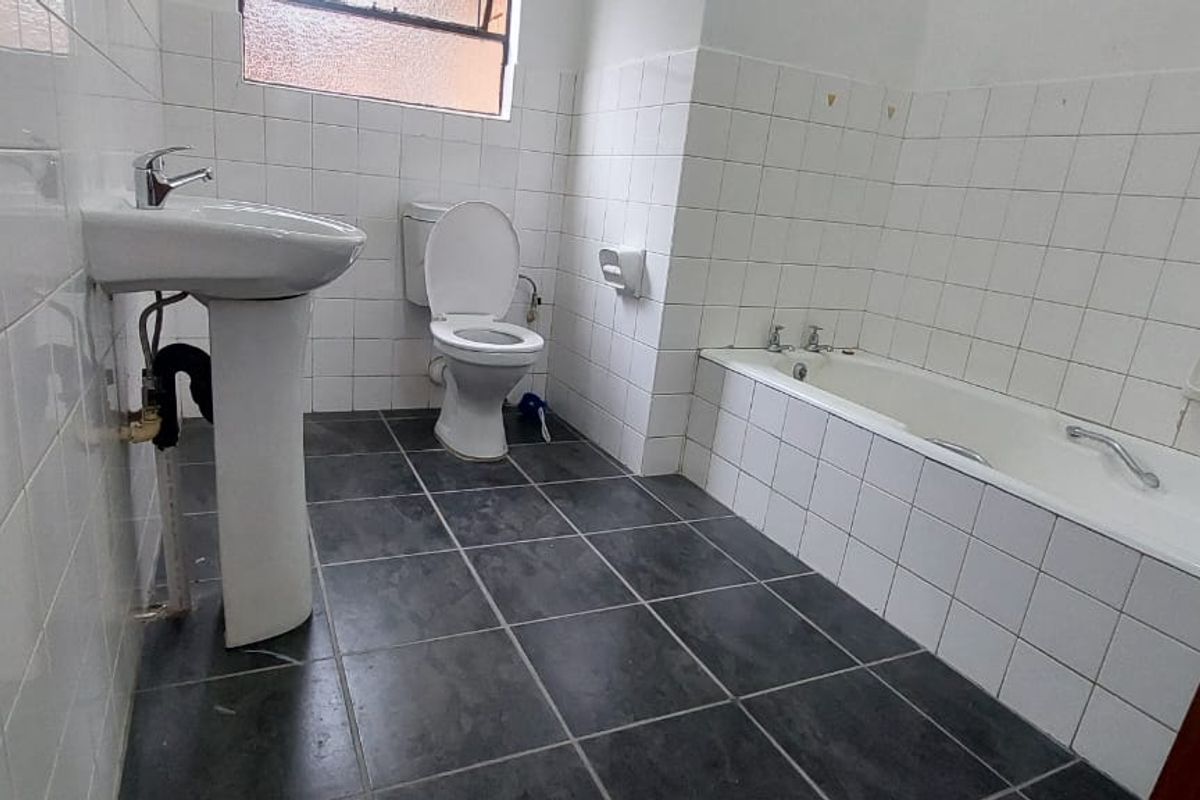 A functional bathroom featuring a pedestal basin, a standard toilet, and a built-in bathtub with white wall tiling and dark floor tiles.