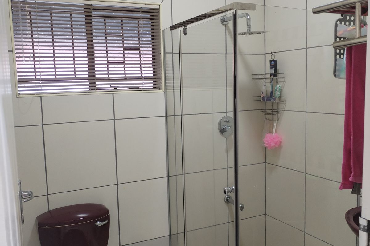 A functional bathroom featuring a glass-enclosed shower, tiled walls, and a dark-toned toilet.
