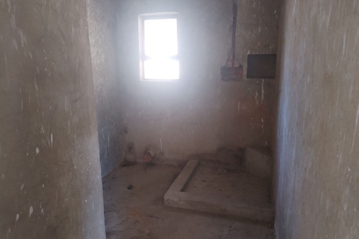 An unfinished bathroom space in shell condition, featuring exposed concrete walls, a built-in shower base, and plumbing rough-ins ready for final installation.