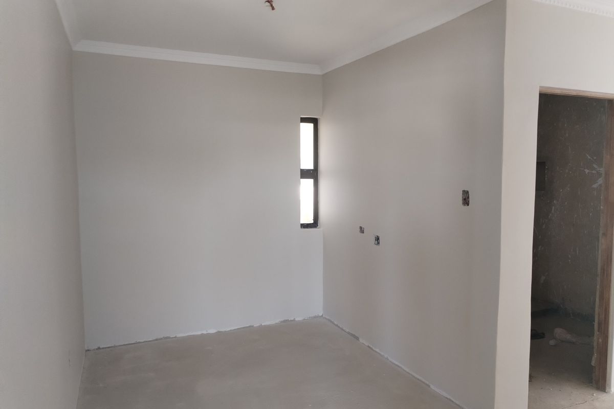 An empty, unfinished bedroom featuring neutral painted walls, crown molding, and a small window, currently awaiting final flooring and electrical fixture installation.