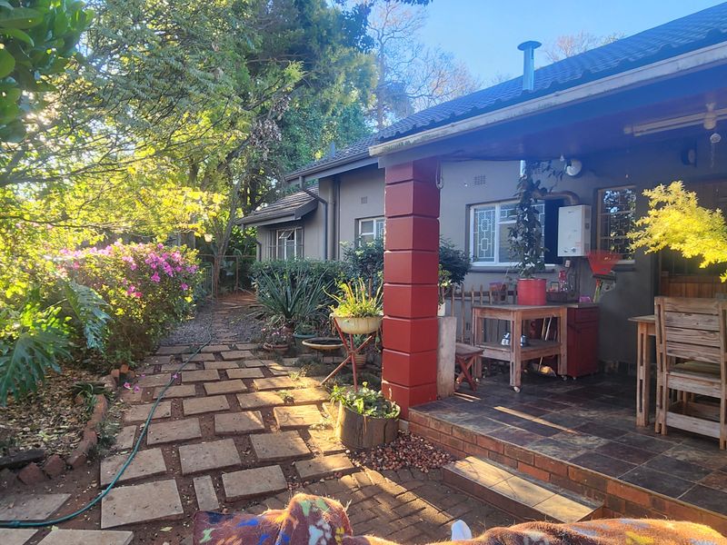A covered patio area featuring tiled flooring and a brick pillar, overlooking a lush, established garden with a paved walkway.