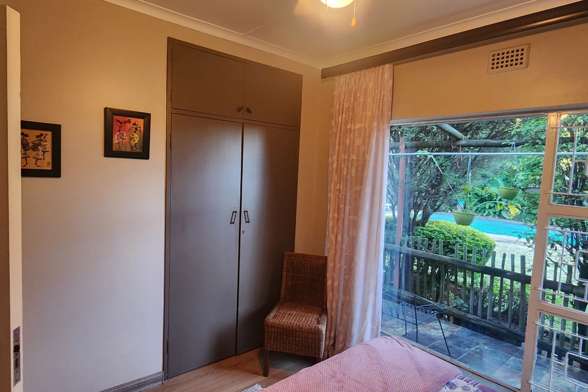 A bedroom featuring built-in cupboards and a large sliding door providing access to the garden and pool area.