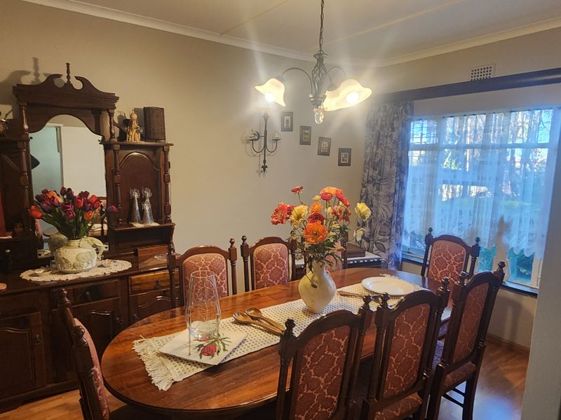 A traditional dining room featuring laminate flooring, a central light fixture, and a large window allowing natural light into the space.