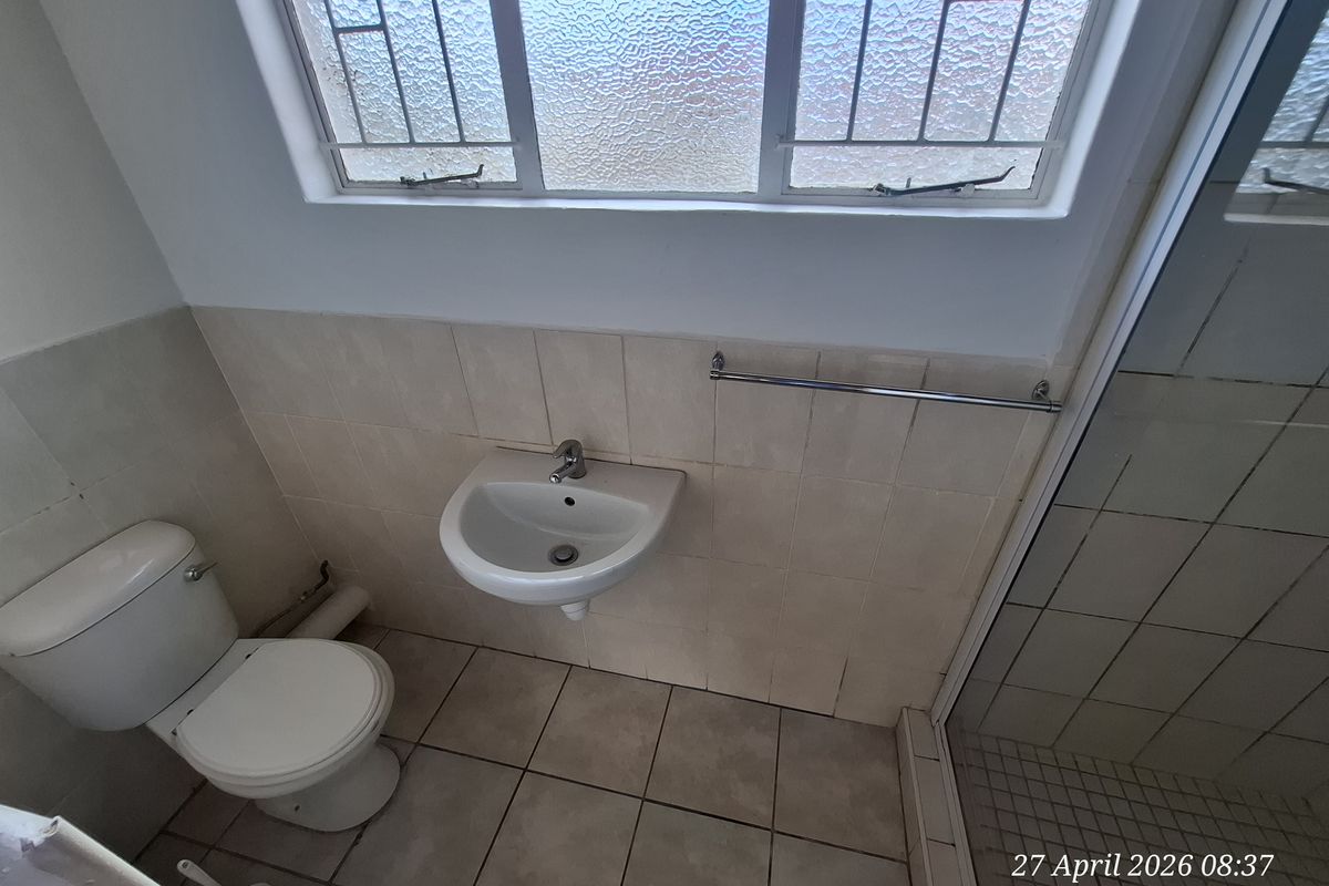 A functional bathroom featuring a wall-mounted basin, toilet, and shower enclosure with tiled finishes and an obscured glass window.