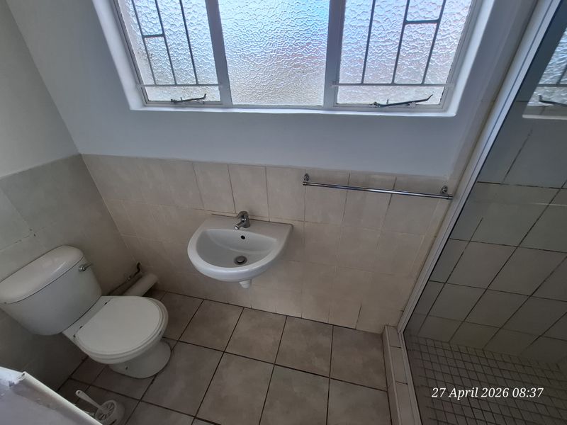 A functional bathroom featuring a wall-mounted basin, toilet, and shower enclosure with tiled finishes and an obscured glass window.