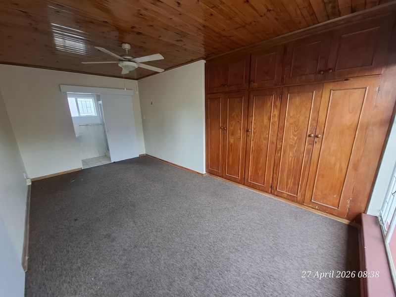 A spacious bedroom featuring extensive built-in wooden cabinetry, a wooden ceiling with a fan, and carpeted flooring, offering a blank canvas for renovation.