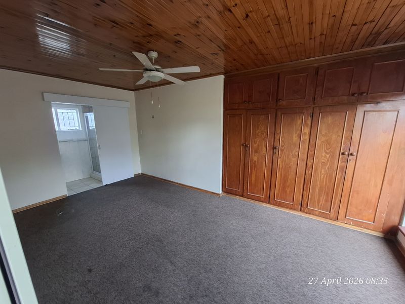 Spacious bedroom featuring extensive built-in wooden cabinetry, a classic wooden ceiling with a fan, and direct access to an en-suite bathroom.