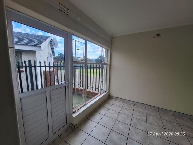 An empty, tiled sunroom or enclosed patio area featuring large windows with security bars and direct access to the exterior.