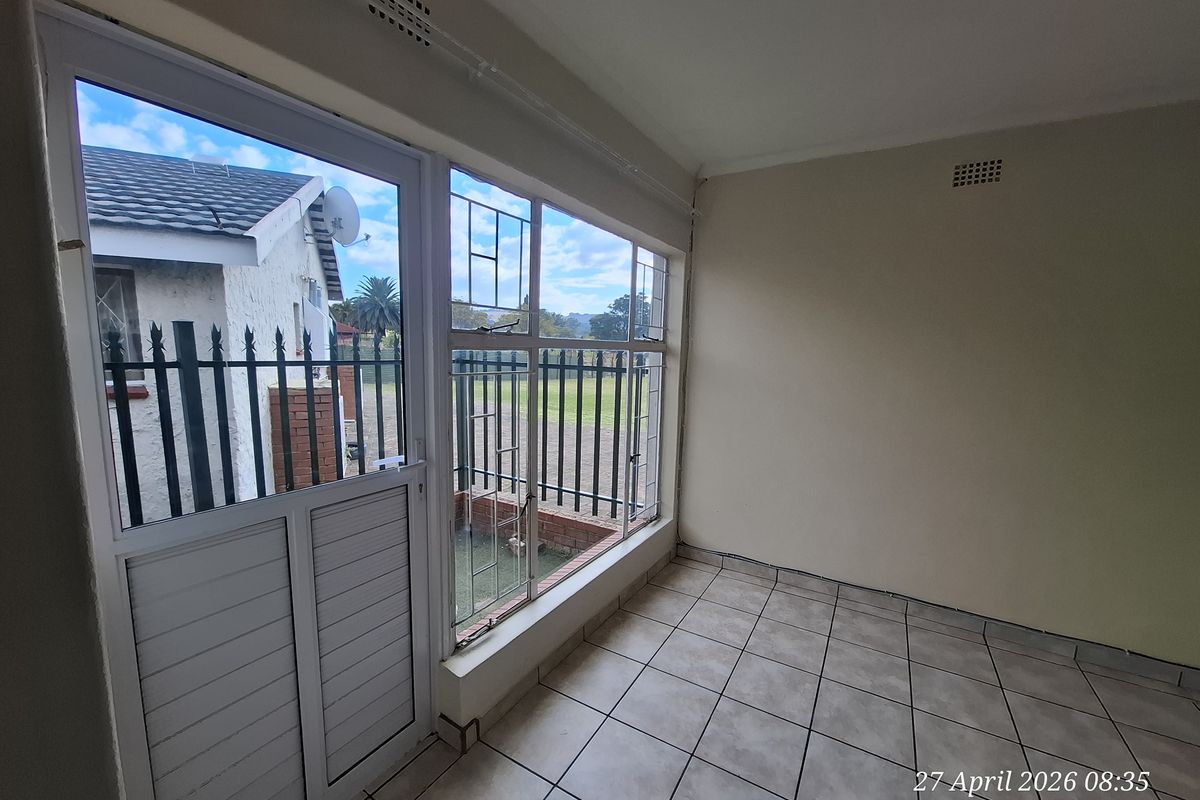 An empty, tiled sunroom or enclosed patio area featuring large windows with security bars and direct access to the exterior.