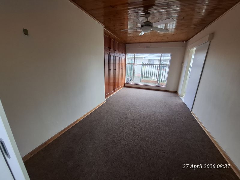 An empty bedroom featuring built-in wooden cupboards, a timber ceiling with a fan, and carpeted flooring, offering a blank canvas for renovation.