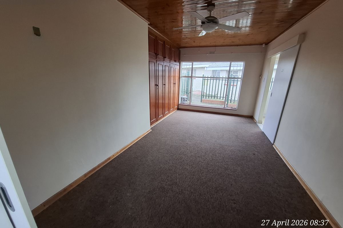 An empty bedroom featuring built-in wooden cupboards, a timber ceiling with a fan, and carpeted flooring, offering a blank canvas for renovation.