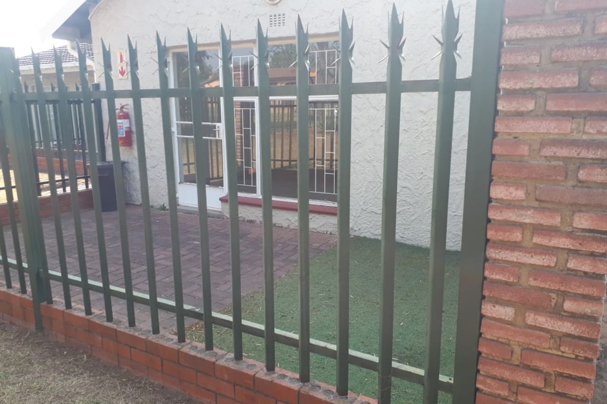 A secure rear patio area featuring paved flooring, enclosed by a brick and metal security fence with integrated security bars on the windows.