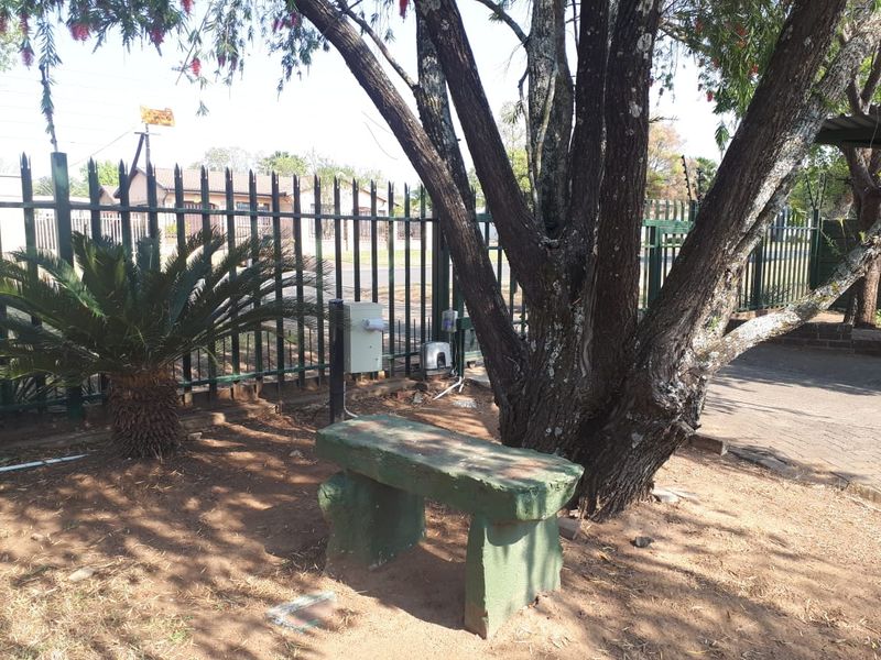 A garden area featuring mature trees, metal security fencing, and an electric gate motor, providing a functional outdoor space.