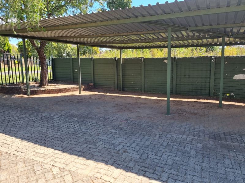 A covered parking area featuring a corrugated metal roof, steel support structure, and paved flooring, enclosed by a precast concrete boundary wall.