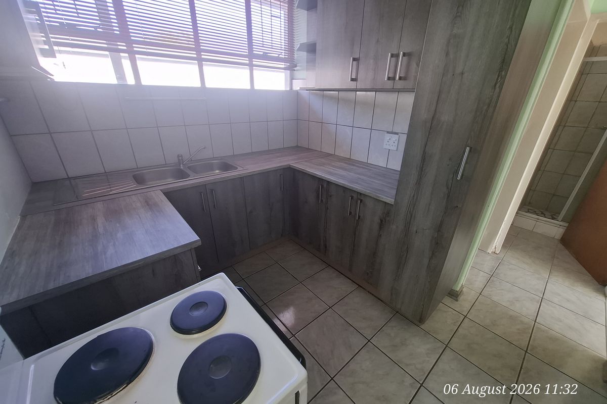 A functional kitchen featuring modern grey laminate cabinetry, ample countertop workspace, a double bowl stainless steel sink, and tiled flooring.