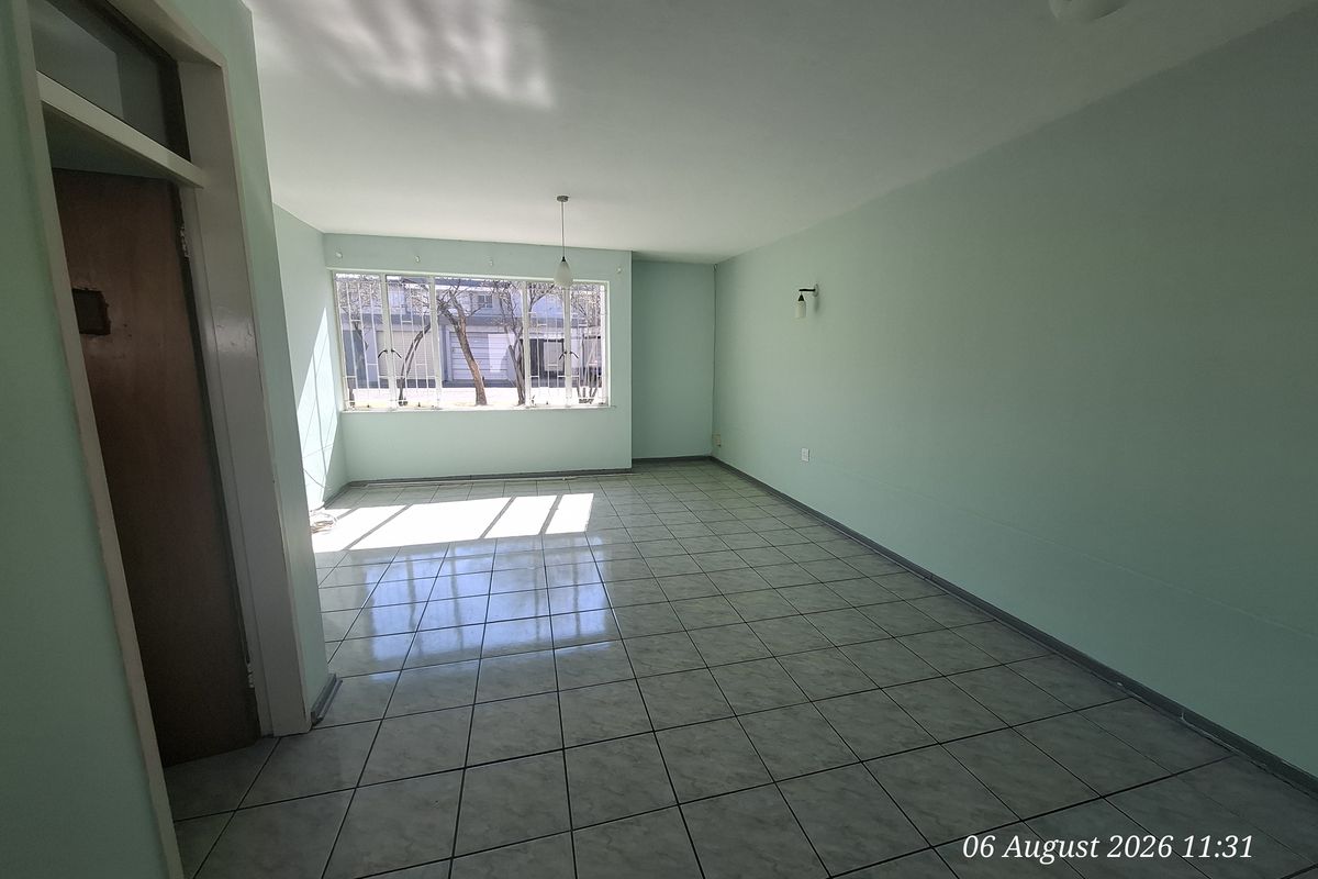 A bright, empty living room featuring neutral tiled flooring and large windows, providing a clean and versatile space ready for personalization.
