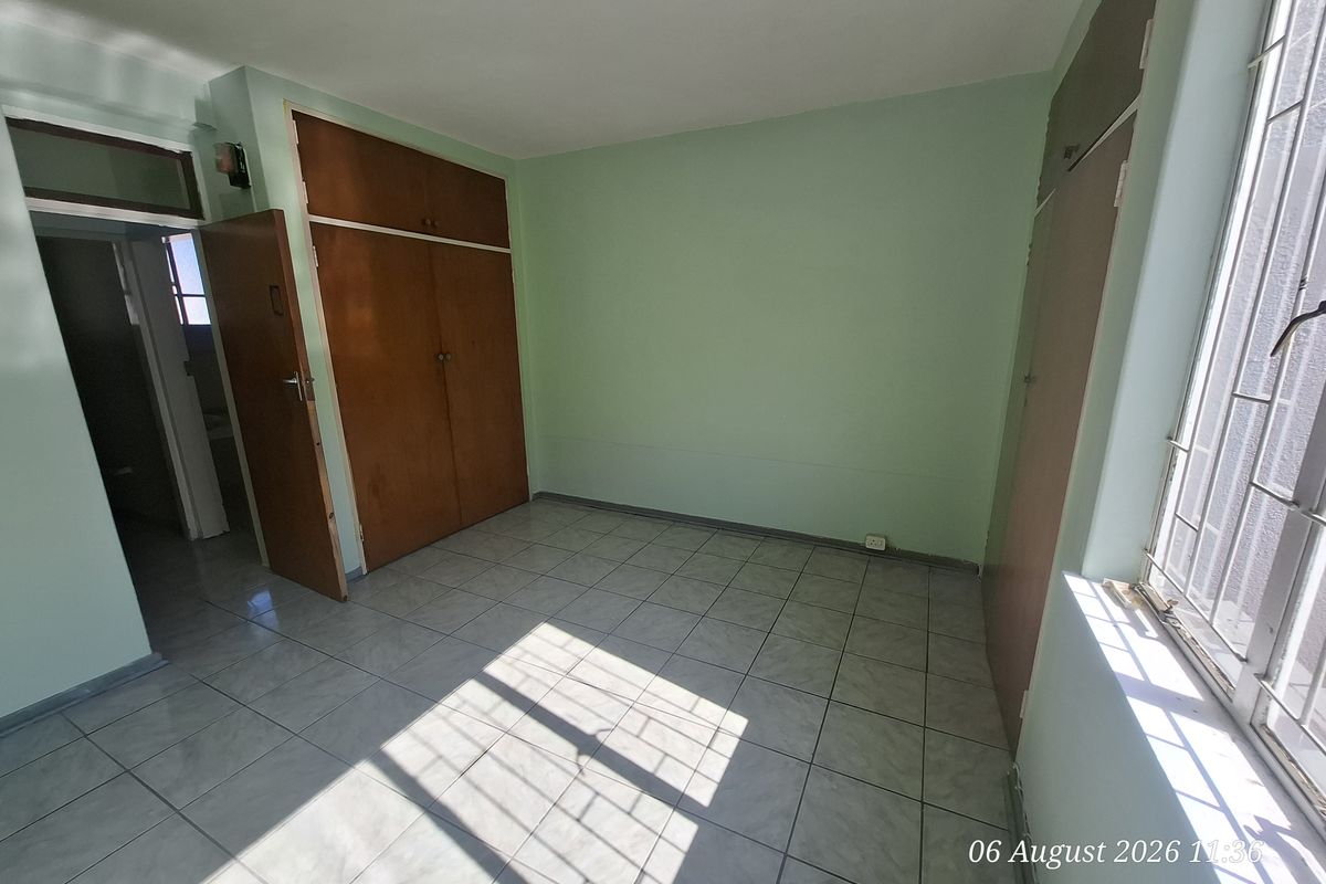 An empty bedroom featuring tiled flooring, built-in wooden cupboards, and a window with security bars.