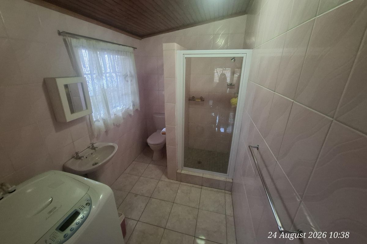 A functional bathroom featuring a shower enclosure, pedestal basin, toilet, and tiled finishes with a timber ceiling.