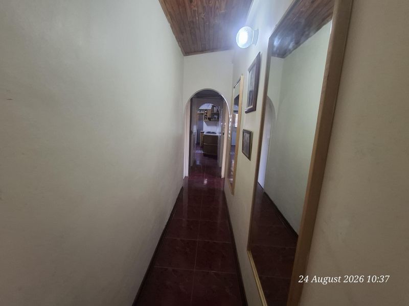 A narrow hallway featuring tiled flooring, a timber-paneled ceiling, and an arched doorway leading to the kitchen area.