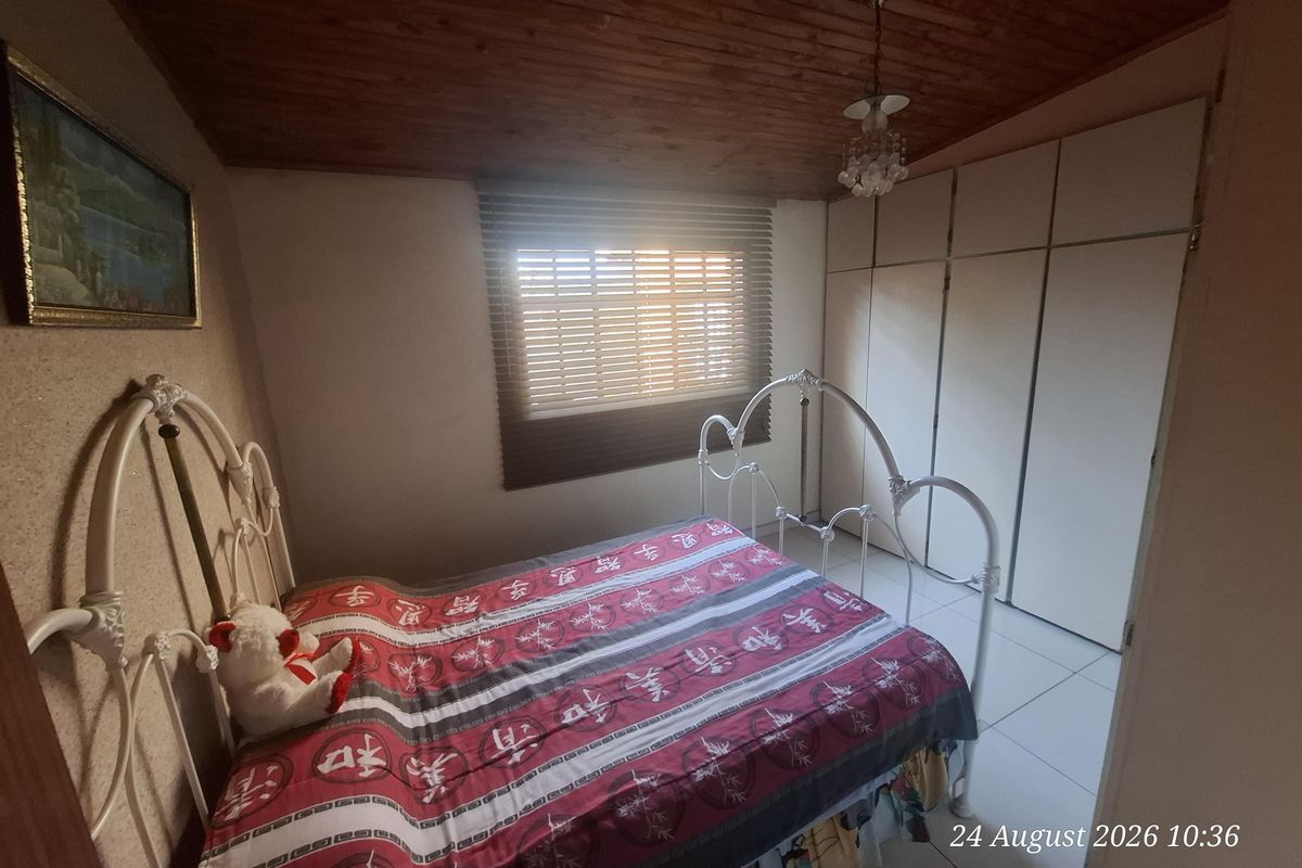 A bedroom featuring built-in cupboards, tiled flooring, and a wooden ceiling, providing a functional space with natural light through venetian blinds.