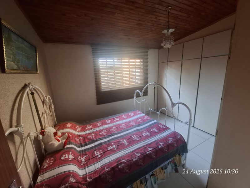 A bedroom featuring built-in cupboards, tiled flooring, and a wooden ceiling, providing a functional space with natural light through venetian blinds.