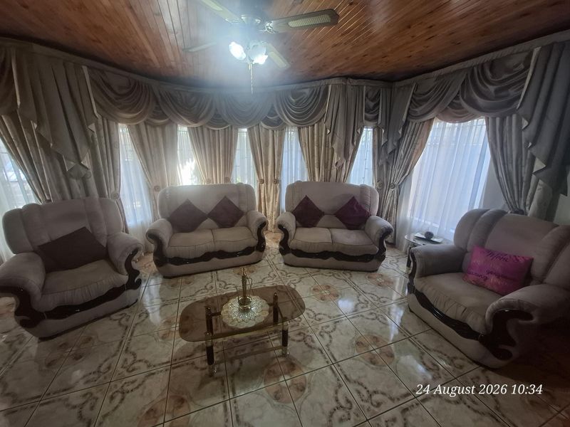 A living room featuring a timber tongue and groove ceiling, ceiling fan, and patterned ceramic floor tiles.