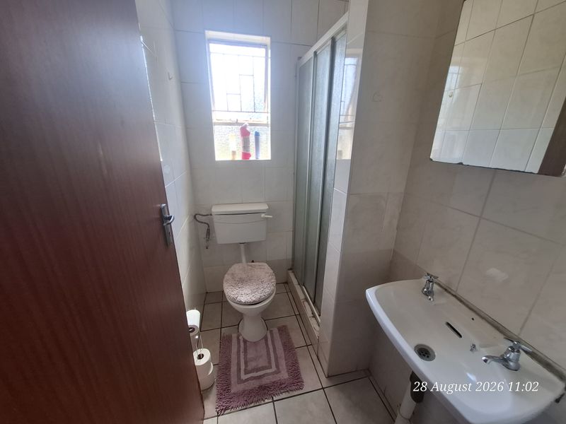 A compact bathroom featuring a shower enclosure, pedestal basin, and toilet, finished with ceramic wall and floor tiles.