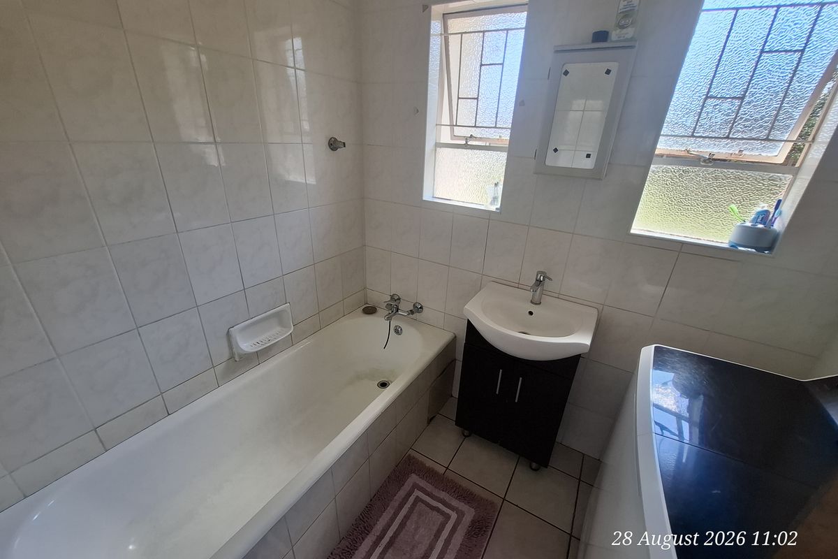 A functional bathroom featuring a bathtub, vanity basin, and tiled finishes, with natural light provided by two windows.
