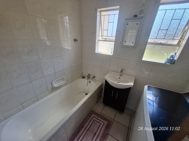 A functional bathroom featuring a bathtub, vanity basin, and tiled finishes, with natural light provided by two windows.