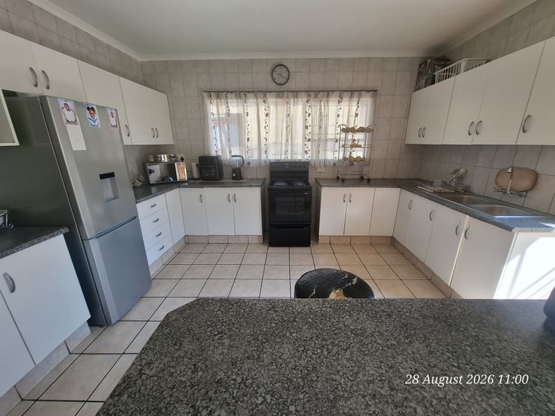 A functional kitchen featuring white cabinetry, laminate countertops, a double basin sink, and a freestanding stove with tiled flooring and splashbacks.