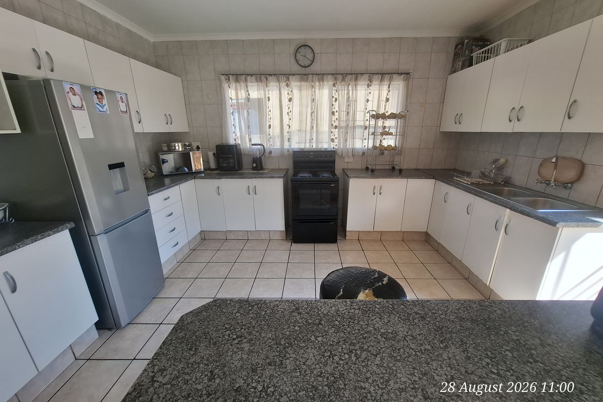 A functional kitchen featuring white cabinetry, laminate countertops, a double basin sink, and a freestanding stove with tiled flooring and splashbacks.