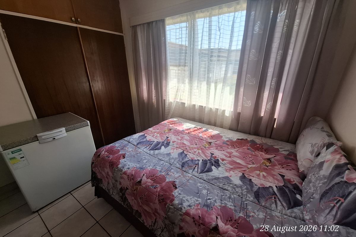 A functional bedroom featuring built-in wooden cupboards and tiled flooring, providing a practical space with natural light.