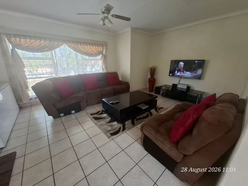 A comfortable living room featuring tiled flooring, a ceiling fan, and large windows with security bars, providing a functional and well-lit space.