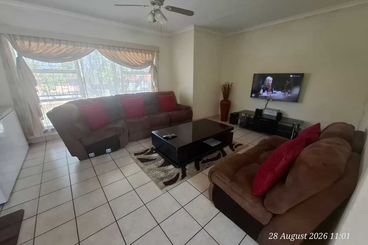 A comfortable living room featuring tiled flooring, a ceiling fan, and large windows with security bars, providing a functional and well-lit space.
