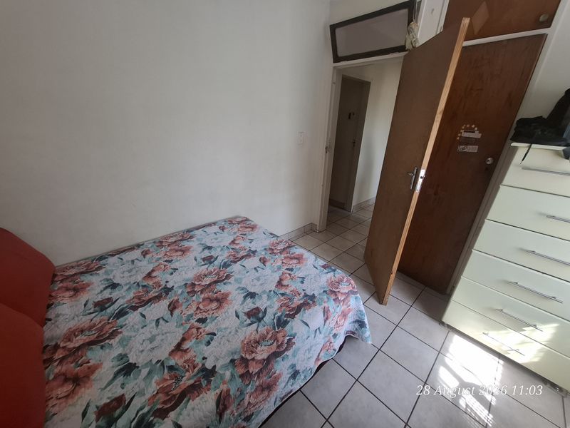 A functional bedroom featuring tiled flooring, a built-in cupboard, and a transom window, providing a basic layout ready for cosmetic updates.
