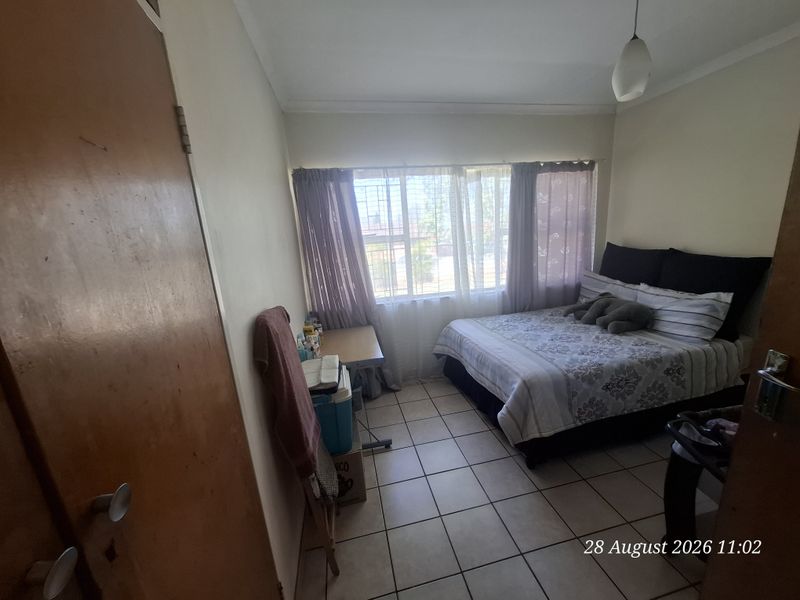 A functional bedroom featuring tiled flooring, a built-in cupboard, and a window with security bars, offering a simple and practical living space.