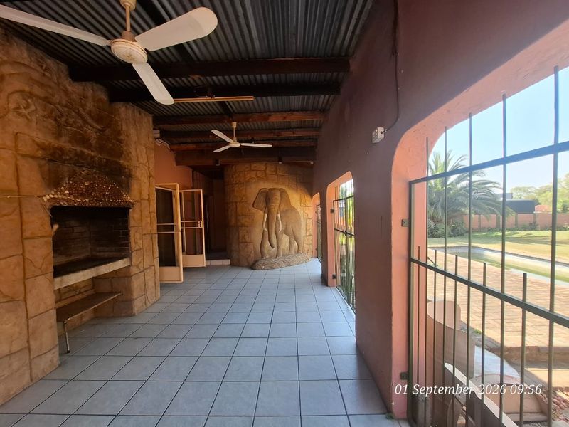 Covered patio area featuring a built-in braai, tiled flooring, and ceiling fans, overlooking the garden and pool area.
