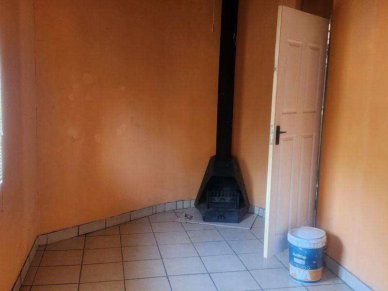 An empty living room featuring tiled flooring, a freestanding fireplace, and venetian blinds, requiring cosmetic updates to the wall finishes.