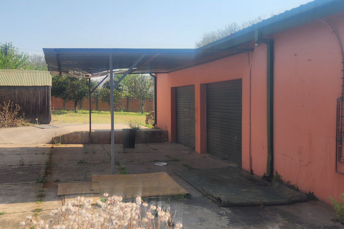 Rear exterior view featuring a covered patio area, double garage with roller shutter doors, and concrete paving in a residential backyard setting.