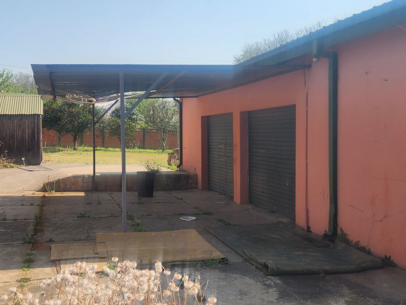Rear exterior view featuring a covered patio area, double garage with roller shutter doors, and concrete paving in a residential backyard setting.